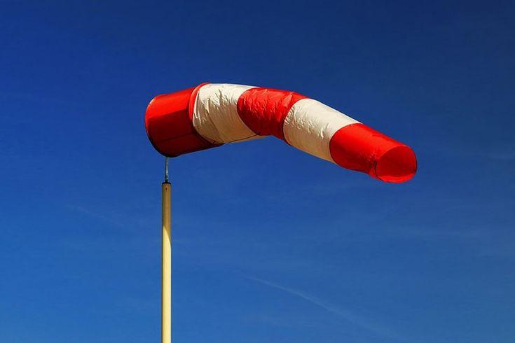 a red and white striped kite flying in the air with a blue sky behind it