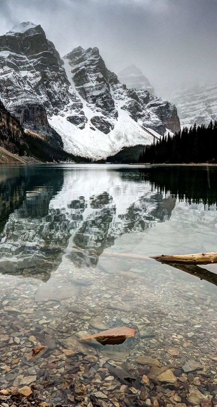 the mountains are covered in snow as they reflect on the still water at the bottom of the lake