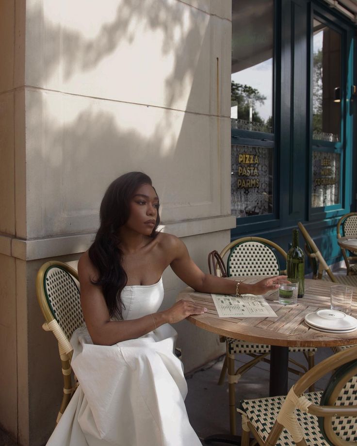 a woman in white dress sitting at table outside