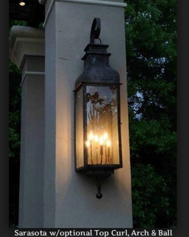 three lit candles are in an old fashioned lantern on the side of a building with trees behind it