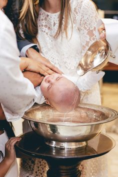 a baby is being washed in a bowl by its mother and father while the woman holds it over her head