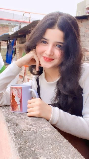 a woman sitting at a table with a coffee mug in her hand and smiling for the camera