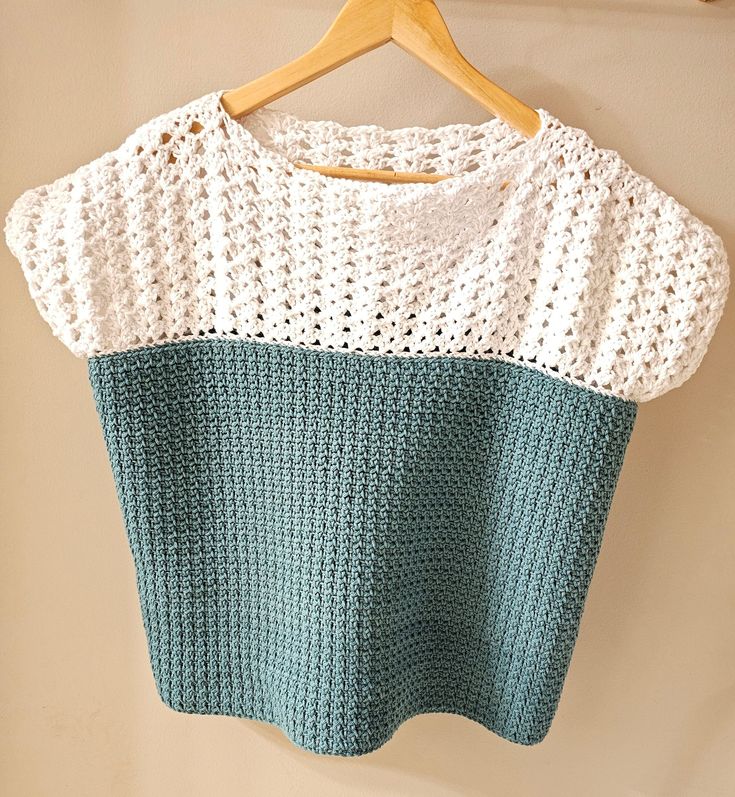 a crocheted top hanging on a wooden hanger next to a white wall