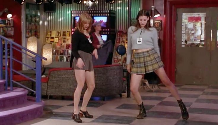 two young women in plaid skirts are dancing on a checkerboard floor while another woman watches