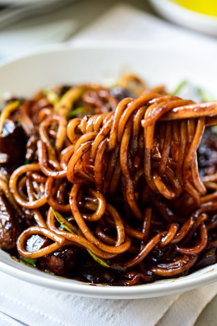 a white bowl filled with noodles and meat on top of a table next to a fork