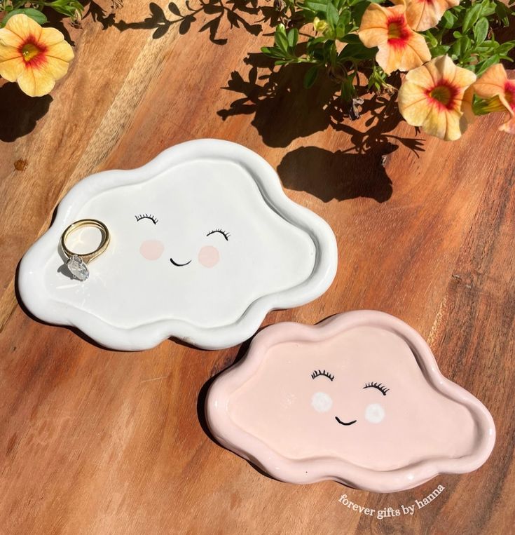 two ceramic clouds with faces on them sitting on a wooden table next to flowers and plants