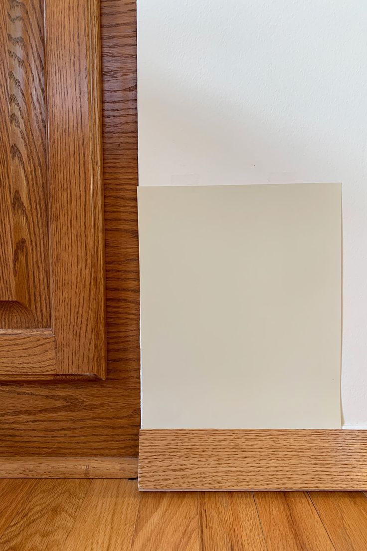 the corner of a room with wood flooring and white paint on the wall next to a door