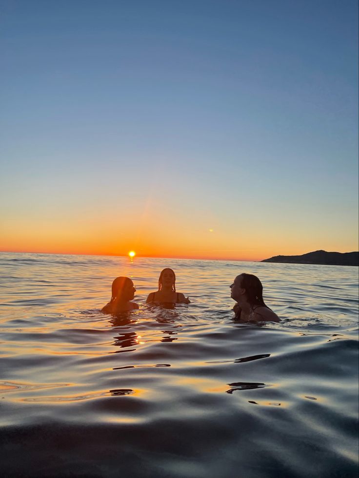 two women are swimming in the ocean at sunset or dawn, with one woman looking back