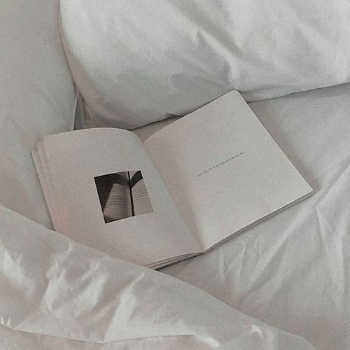 an open book sitting on top of a bed next to white sheets and pillow covers