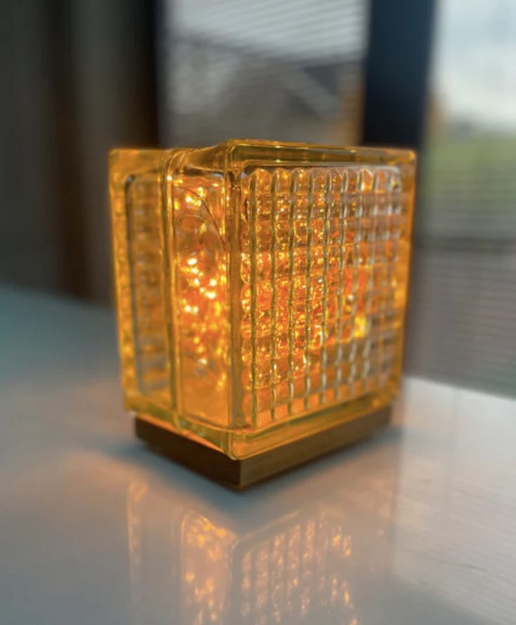 a yellow glass object sitting on top of a white table next to a window in the background