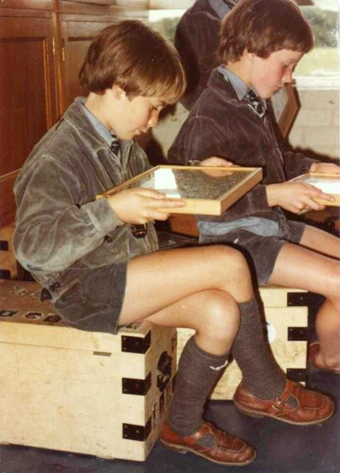 two young boys sitting on top of wooden boxes with books in their hands and one boy reading