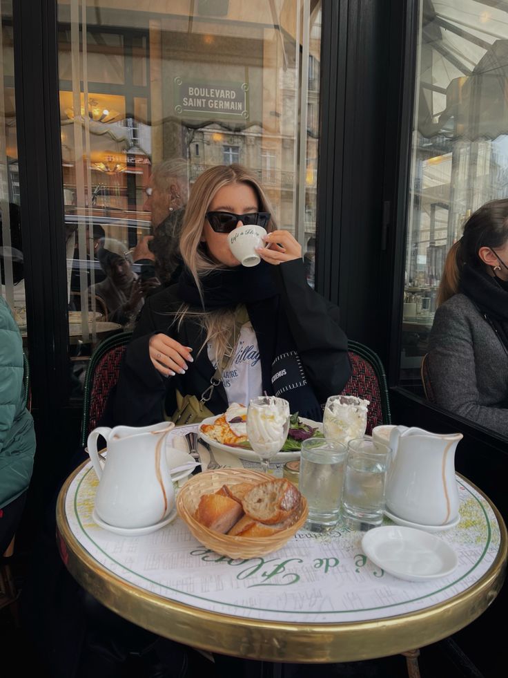 a woman sitting at a table drinking from a coffee cup and eating pastries in front of her