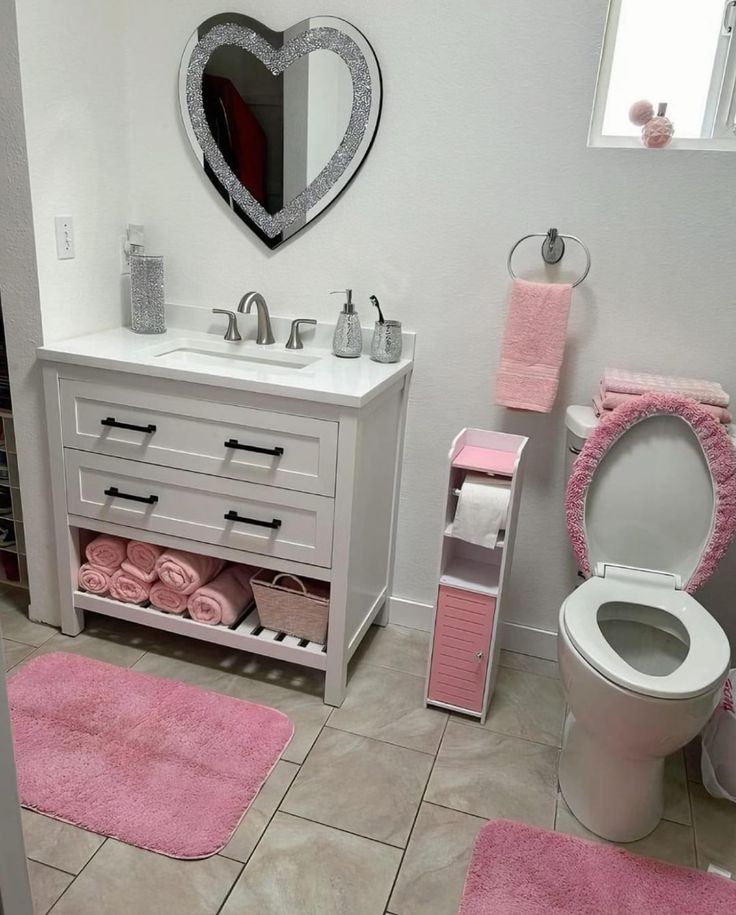 a white bathroom with pink rugs on the floor and towels on the shelf next to the toilet