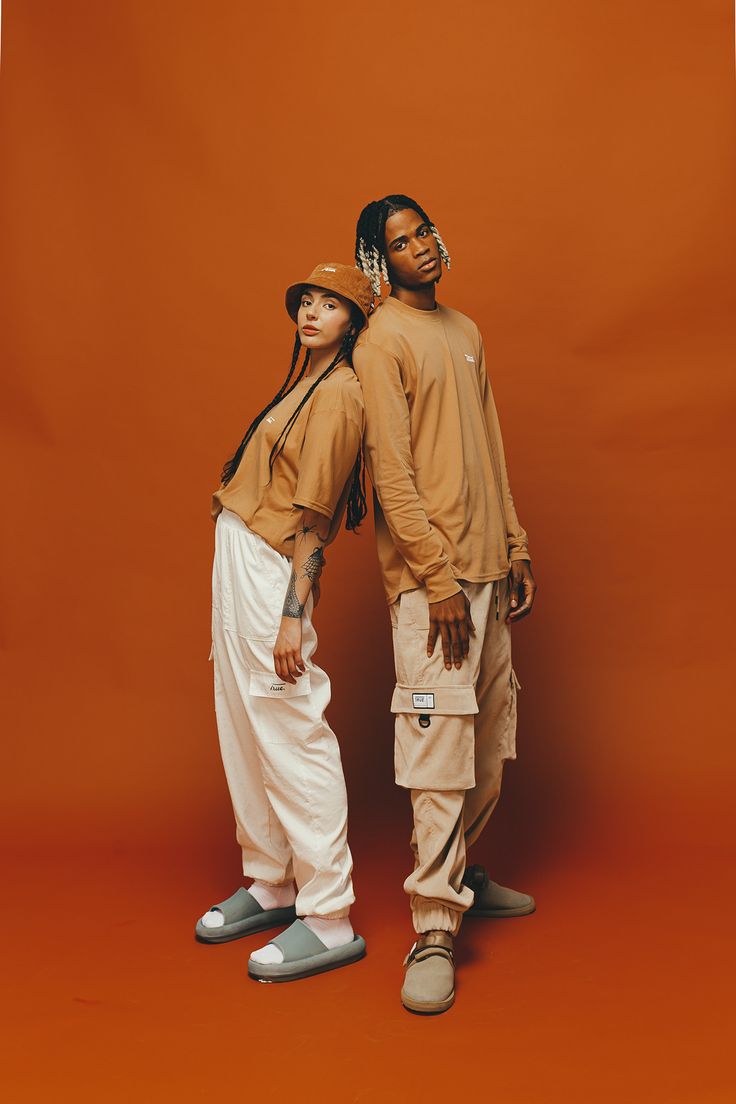 two people standing next to each other in front of an orange background