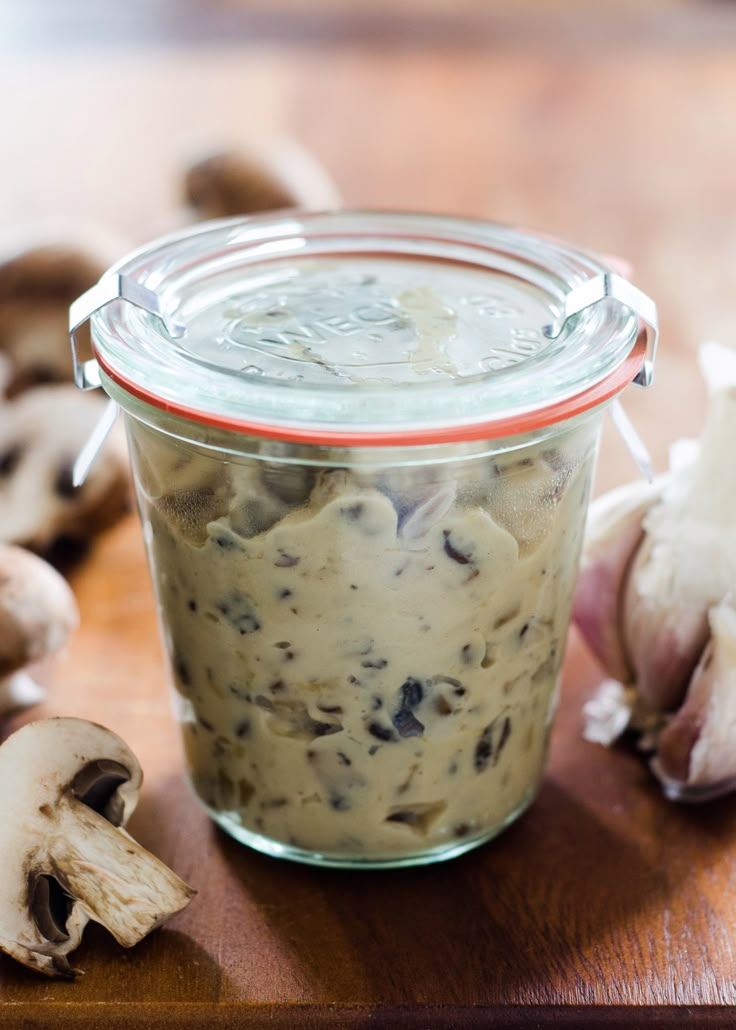 a jar filled with food sitting on top of a wooden table next to garlic and mushrooms