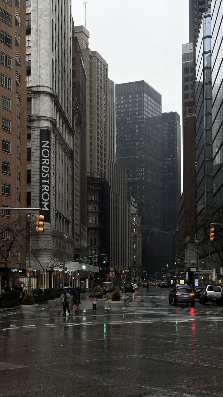 people crossing the street in front of tall buildings on a rainy day with traffic lights