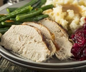 a white plate topped with turkey, mashed potatoes and cranberry sauce next to green beans