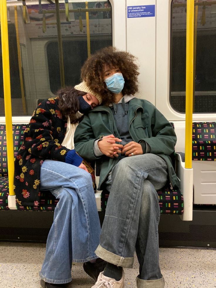 two people sitting on a subway train wearing masks