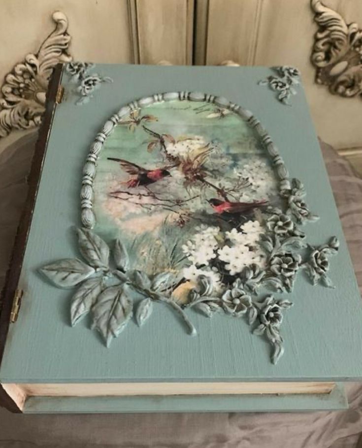 an old book with flowers and birds painted on the cover is sitting on a chair