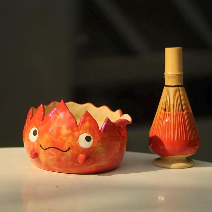 an orange vase sitting on top of a white table next to a red glass bottle