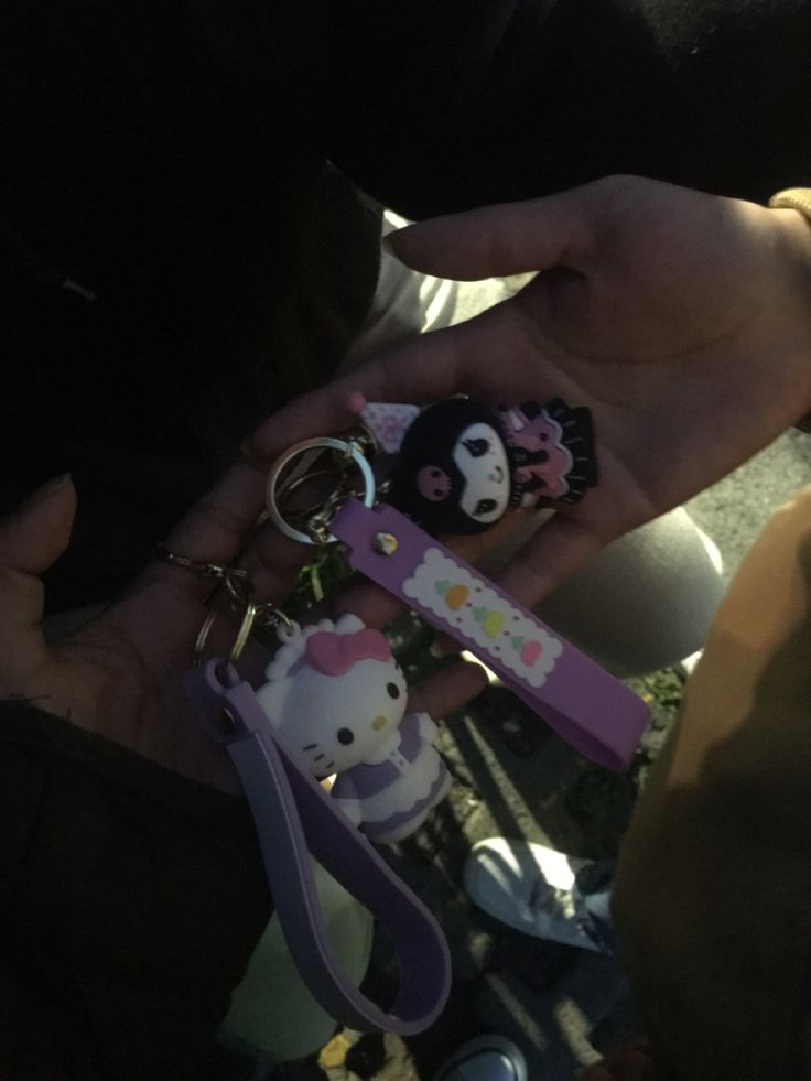 two people holding hello kitty keychains in their hands and one person is holding a cell phone