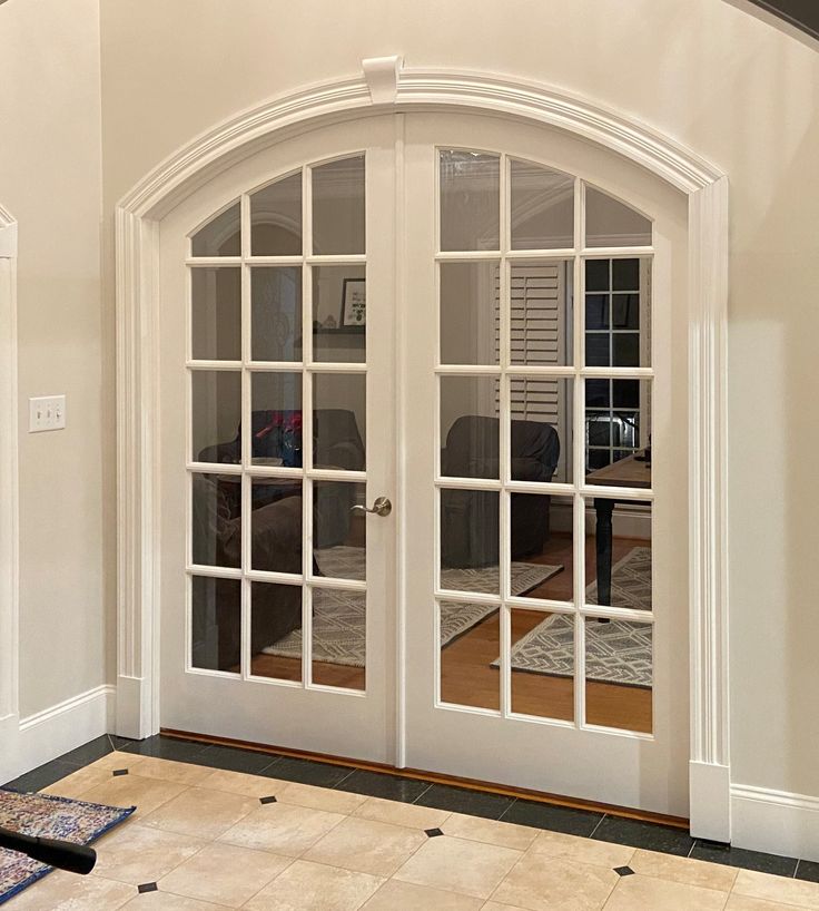 an arched glass door leading to a living room with beige walls and tile flooring