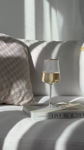 a glass of wine sitting on top of a bed next to a book and lamp