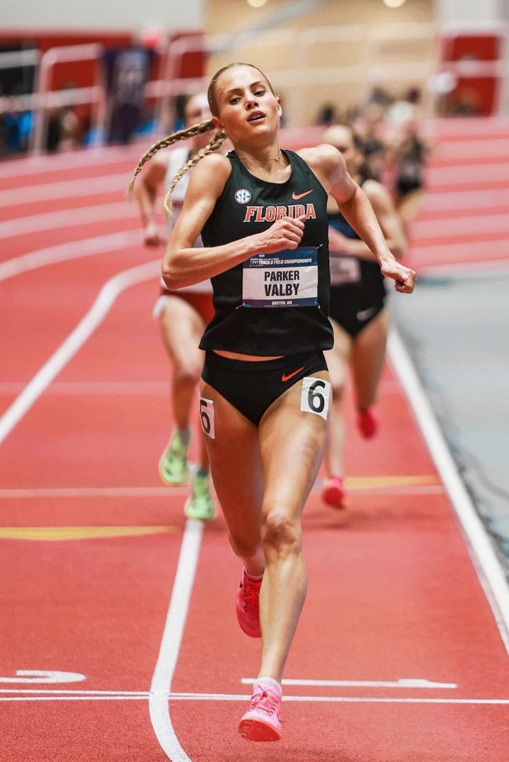 a woman running on a track with other people in the background