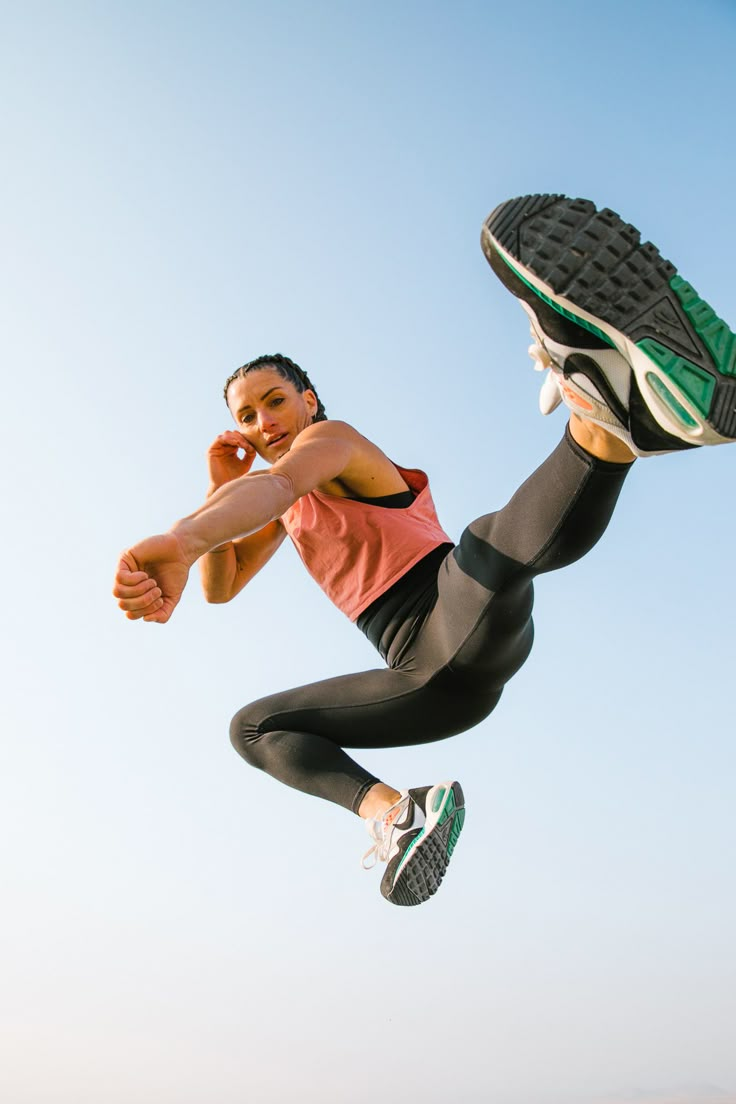 a woman is jumping in the air with her feet up and wearing running shoes on