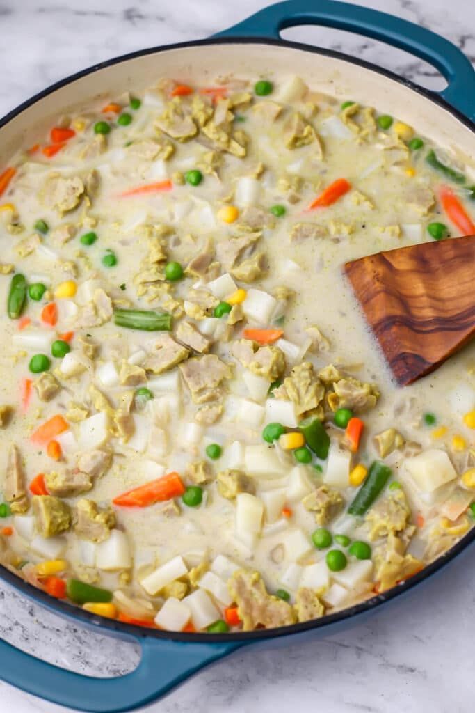 a pot filled with chicken and vegetables on top of a marble countertop next to a wooden spoon