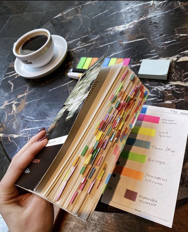 a person holding an open book on top of a table next to a cup of coffee