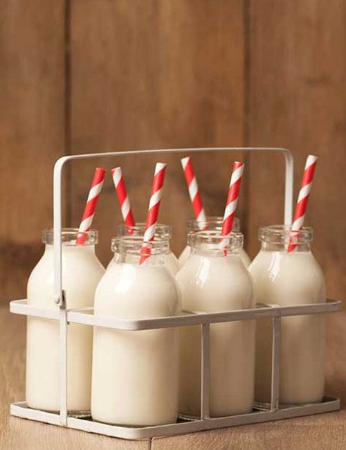 six bottles of milk with red and white striped straws in them on a wooden table