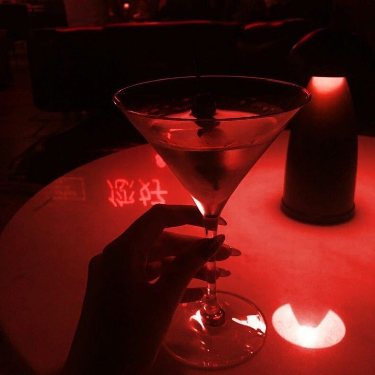 a person is holding a martini glass in front of a red light at a restaurant