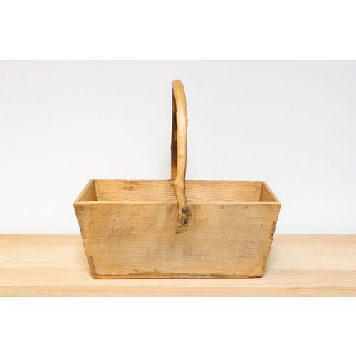 a wooden basket sitting on top of a table next to a white wall and floor