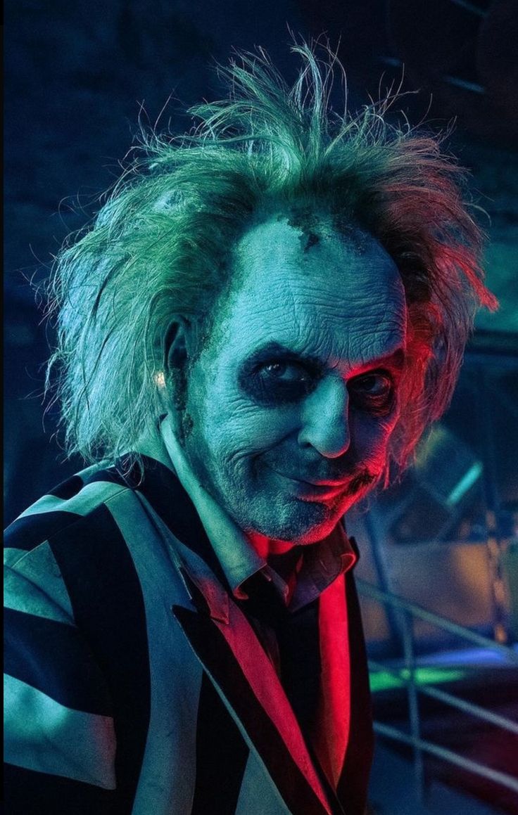 a man dressed as the joker with green hair and red eyes is standing in front of a stage