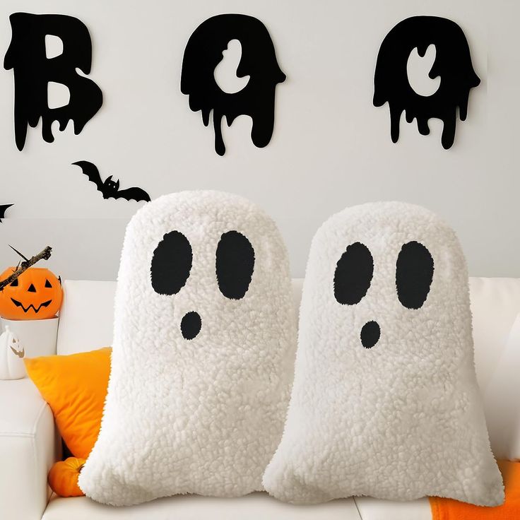 two pillows with ghost faces on them sitting in front of a white couch and halloween decorations