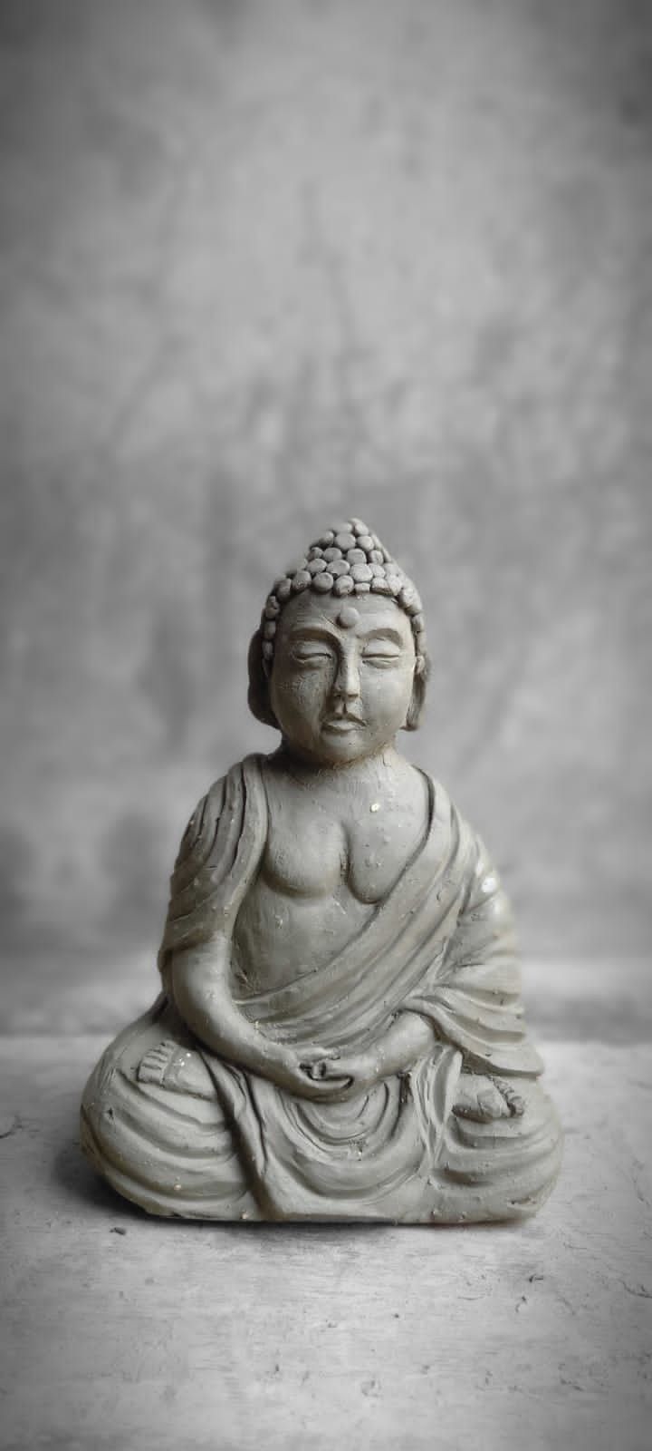 a buddha statue sitting on top of a white table next to a gray wall with a black and white background