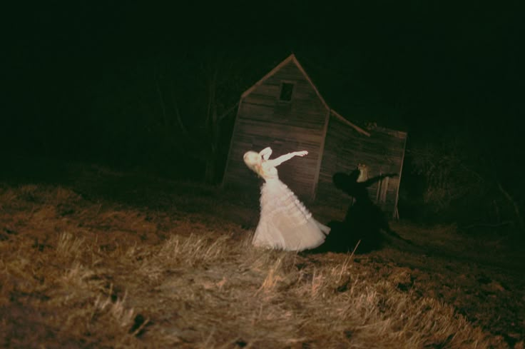 a woman in a white dress standing next to a wooden shed on top of a hill