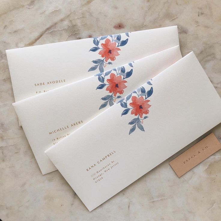 three envelopes with red flowers on them sitting on a marble counter top next to a business card