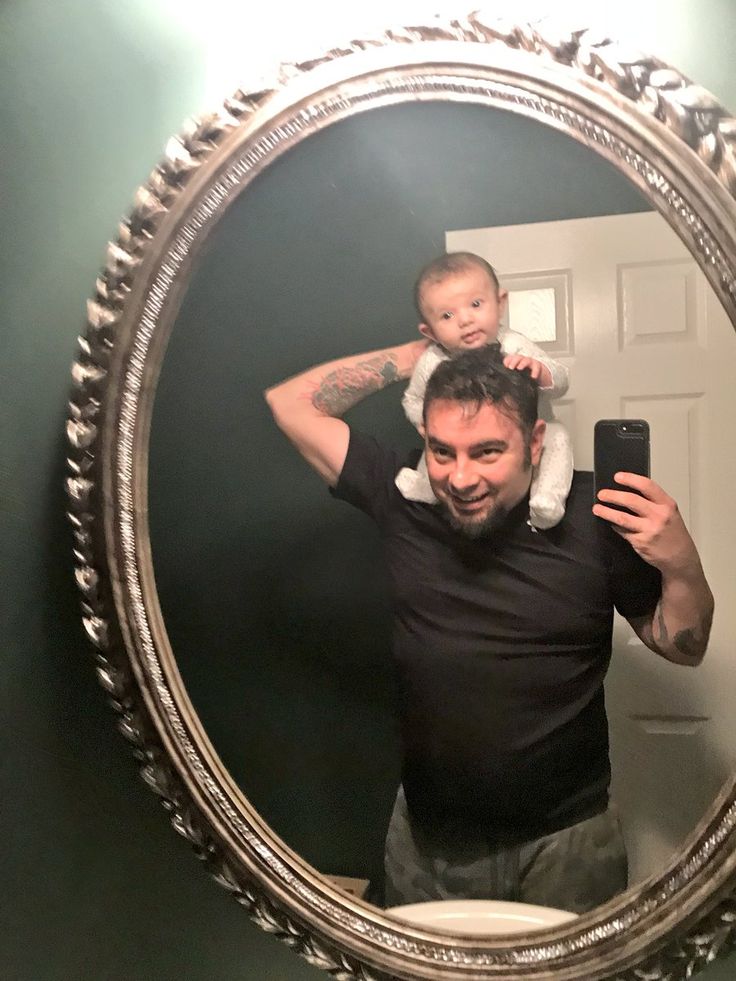 a man taking a selfie in front of a mirror with a baby on his shoulders