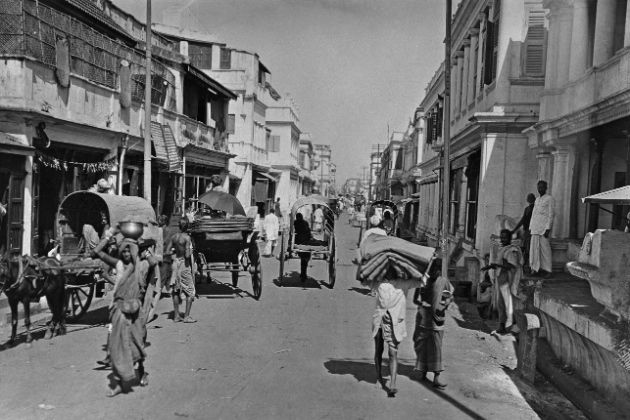 an old black and white photo of people walking down the street with horse drawn carriages