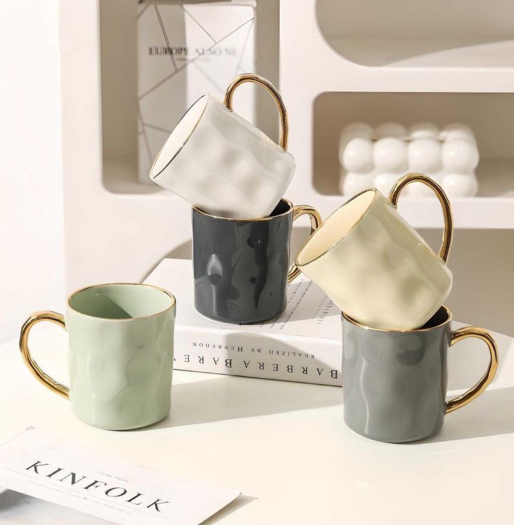 four coffee mugs sitting on top of a white table next to a book and magazines