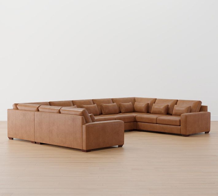 a tan leather sectional sofa sitting on top of a hard wood floor next to a white wall