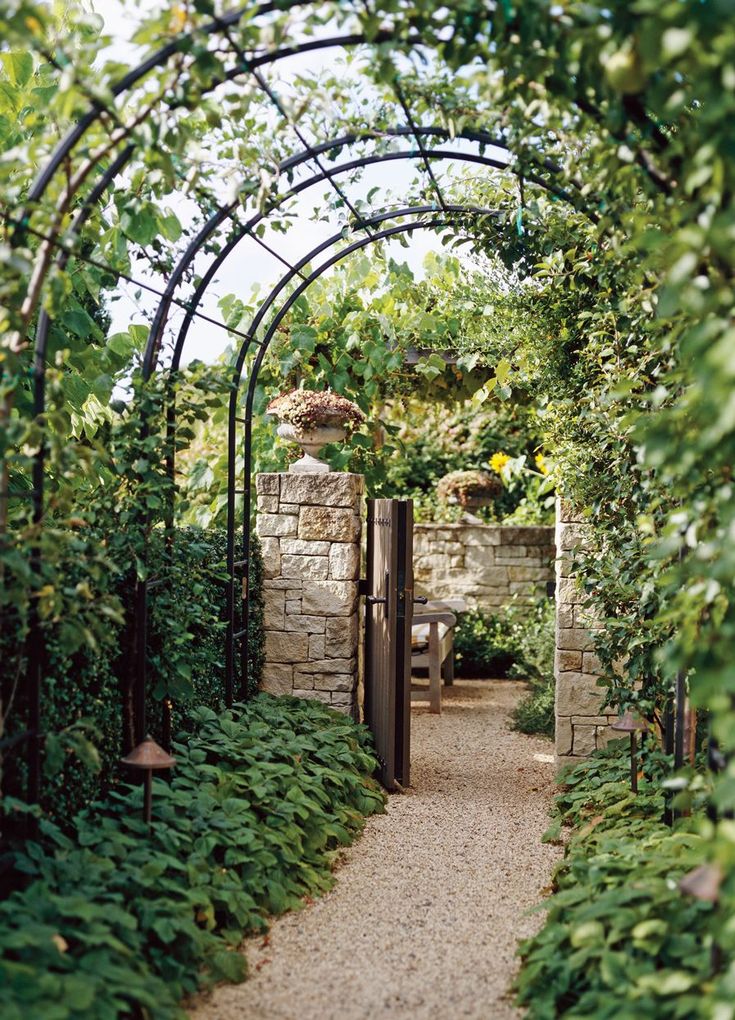 an archway in the middle of a garden with lots of greenery on both sides