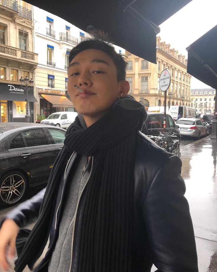 a man standing in front of a building on a rainy day wearing a black jacket and scarf