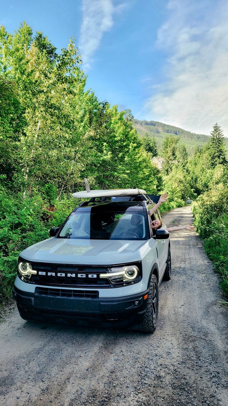 a truck parked on the side of a dirt road in front of trees and bushes