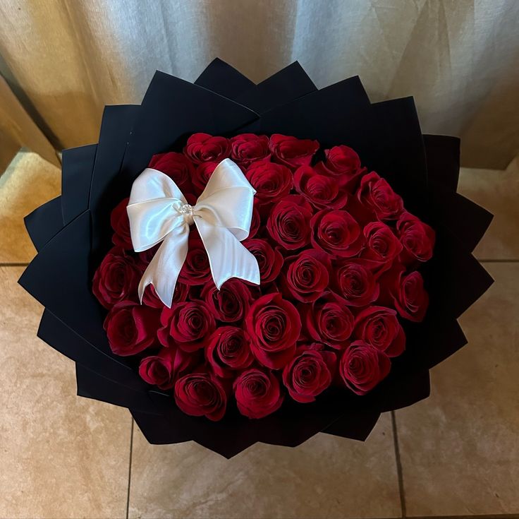 a large bouquet of red roses with a white bow on the top in a black box