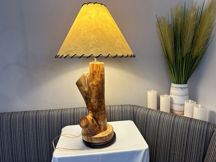 a table lamp sitting on top of a white table next to a gray couch and potted plant