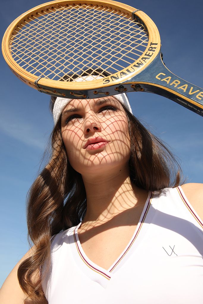 a woman holding a tennis racquet on her head while wearing a white top