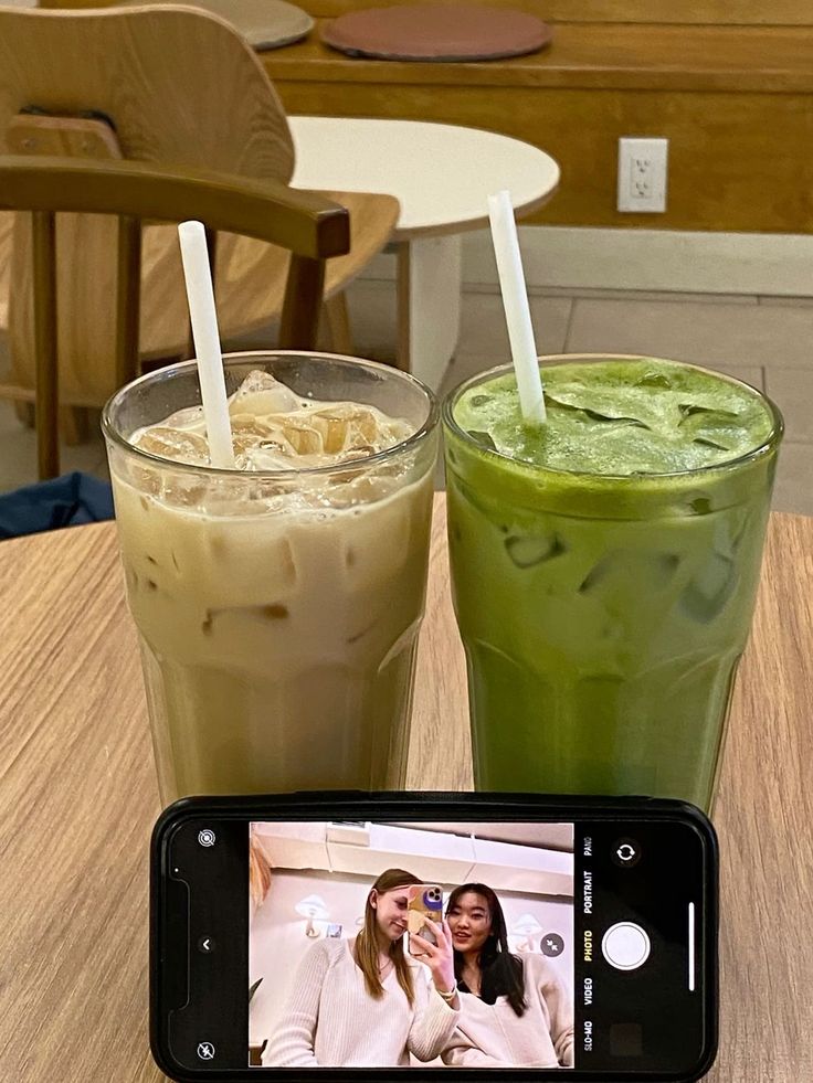 two drinks sitting next to each other on top of a wooden table in front of a cell phone